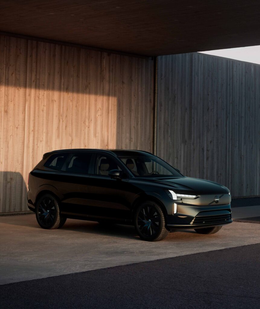 Volvo EX90 Black Edition pysäköitynä puuverhoillun rakennuksen edustalle.