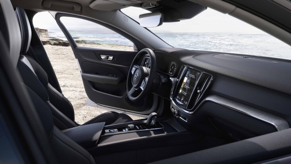 Volvo V60 mustat sisätilat, etualalla kosketusnäyttö, vaihdekeppi sekä ratti, etuovi auki ja taustalla meri.
